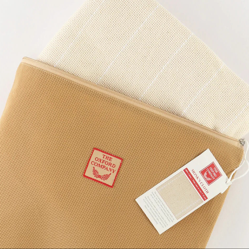 A tan canvas zippered pouch with a red square 'The Onion Company' logo patch, shown partially open with a folded cream woven textile inside. A product tag hangs from the zipper on a clean white background.