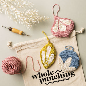 Bright punch needle bauble decorations lying flat on a table with yarn, punch needle and whole punching drawstring bag