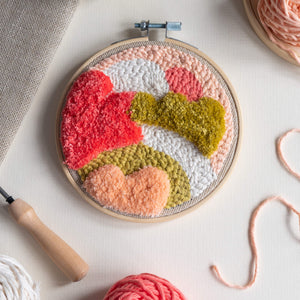 Dune punch needle hoop in coral, white and chartreuse flat on a surface with punch needle, yarn and fabric just coming into shot around the edge