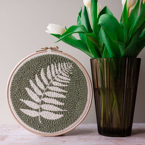 Finished fern punch needle hoop wall hanging next to a vase of tulips