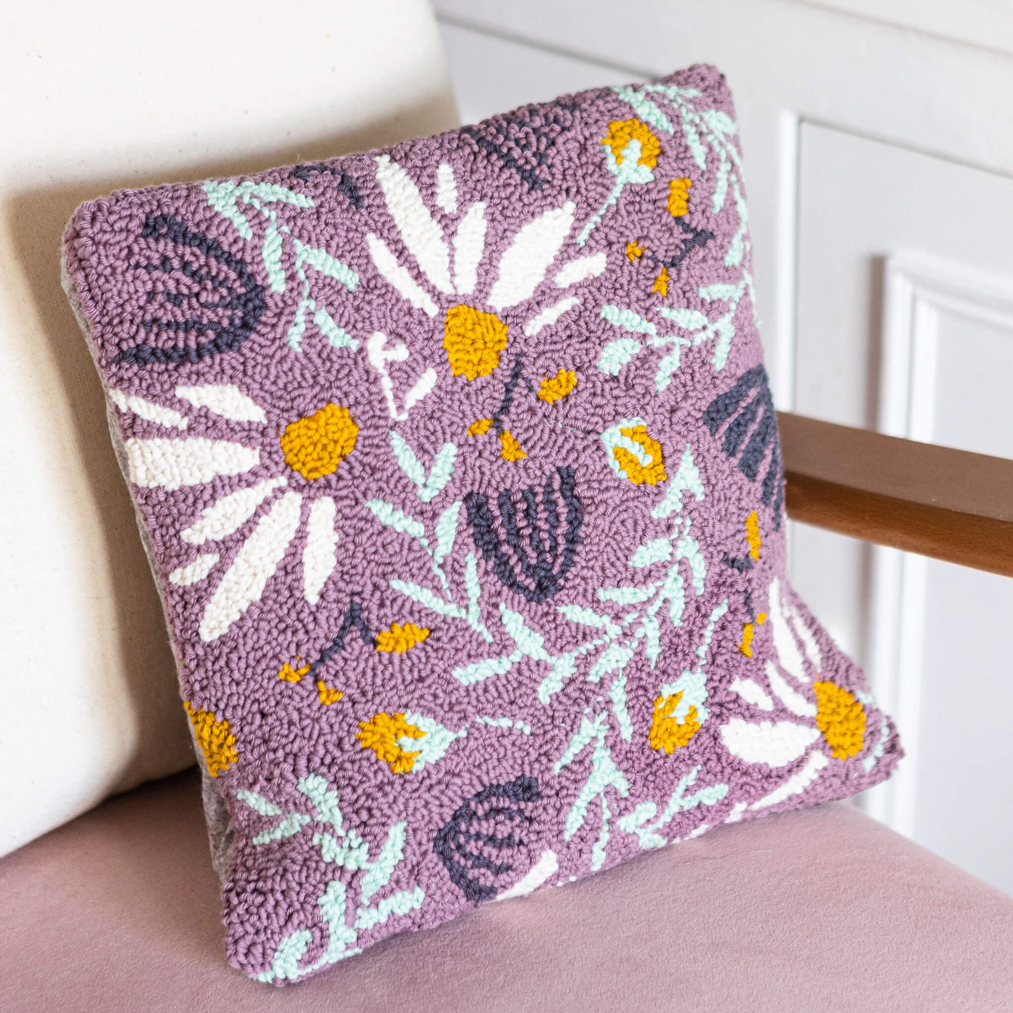 Lilac punch needle floral cushion propped against a pink velvet chair with a light cream cushion