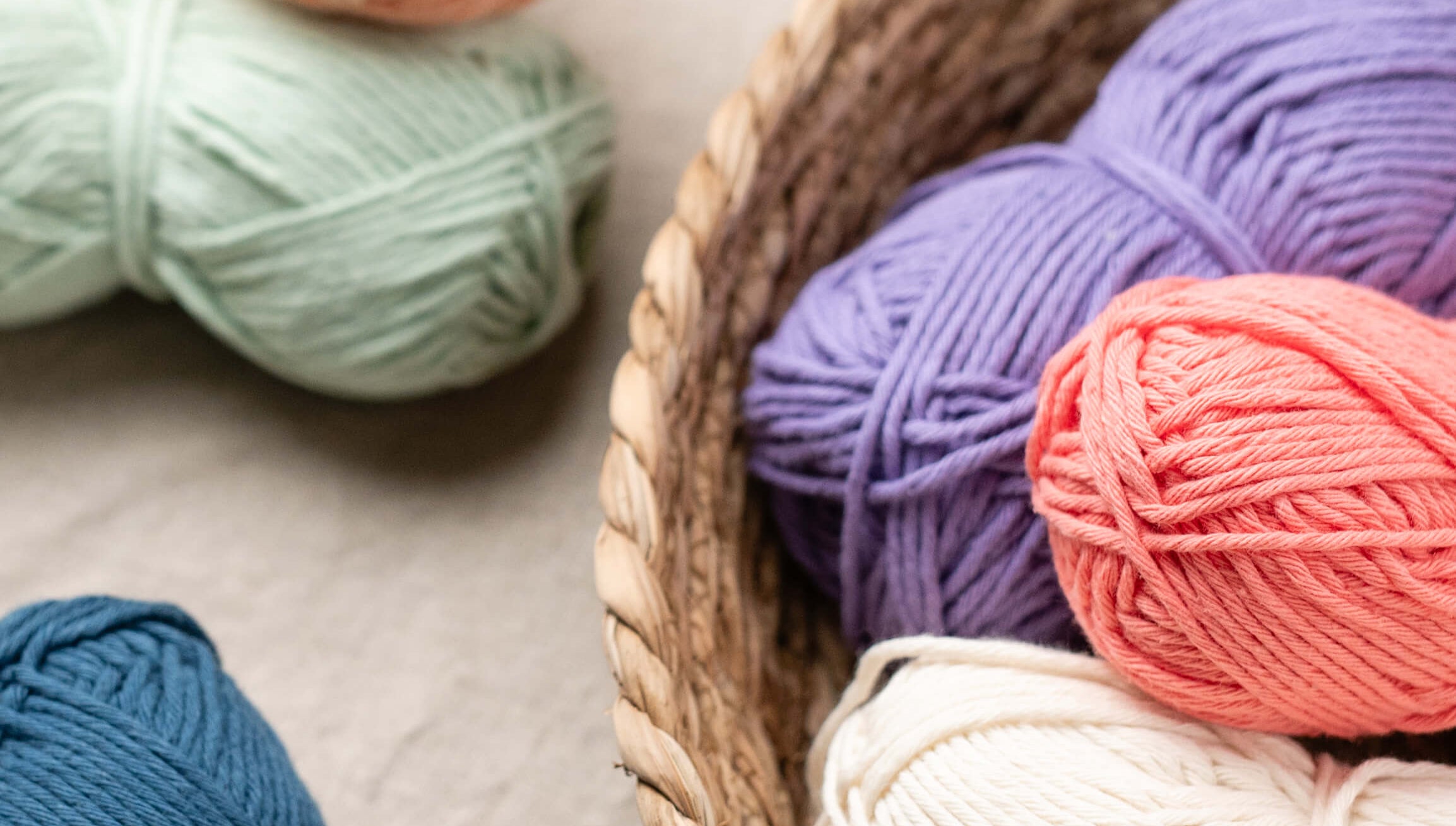 Colorful yarn balls on a textured surface with a woven basket.