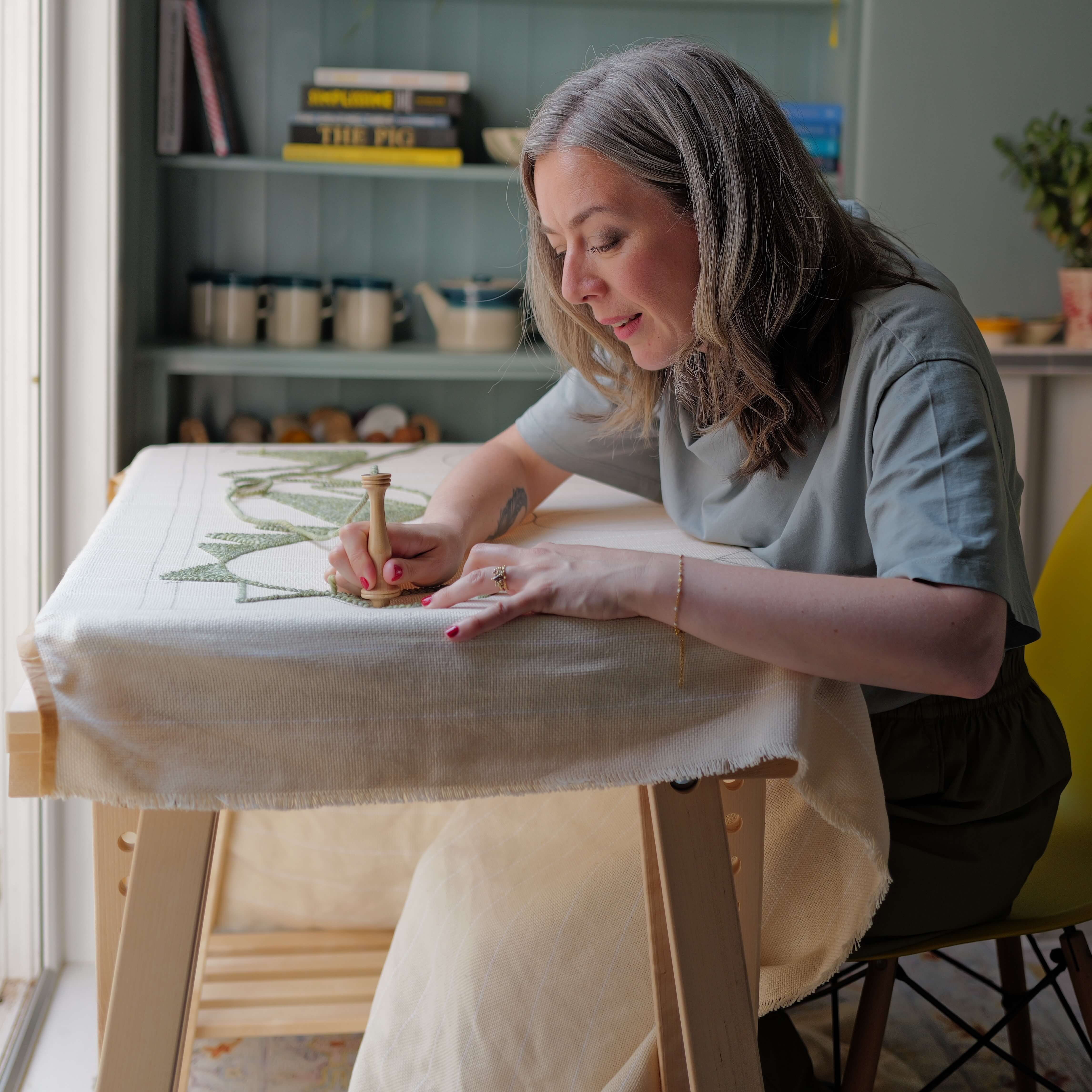 Sara from Whole Punching working on a large punch needle rug in her home

