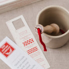 oxford punch needle in ceramic cup with red yarn extending, stitch gauge and quick start guide lay beside it