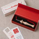 The Oxford Punch Needle kit shown with its red presentation box, white branded box lid, instruction booklet, and a wooden punch needle tool with red cord on a neutral fabric background.