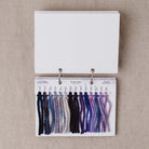 Yarn color swatch book with purple and blue yarn samples on a beige fabric background