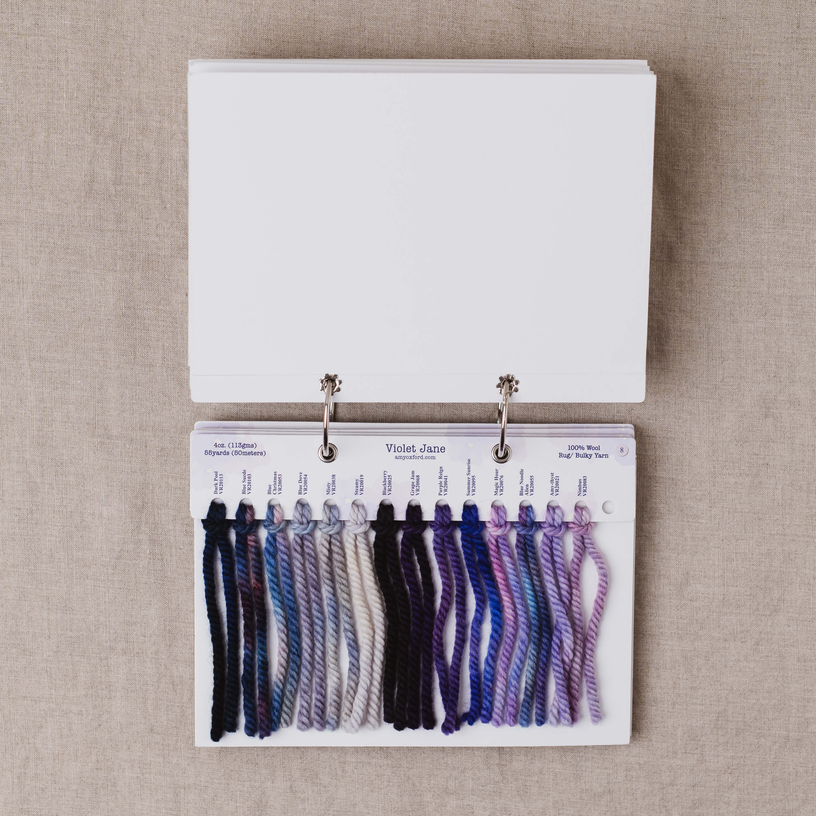 Yarn color swatch book with purple and blue yarn samples on a beige fabric background