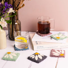 Load image into Gallery viewer, Punch needle coasters in daisy pattern, books to the side with a clear mug of tea propped on a coaster. Vases to the left are just in shot with fresh and dried flowers - the scene has a warm pink glow.