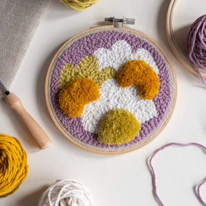 Punch needle and tufted daisy hoop laying flat with punch needle, yarn and fabric coming into focus around edge