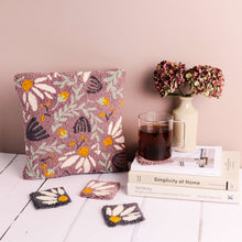 Load image into Gallery viewer, Lilac floral  punch needle cushion against a pink background with punch needle coasters in the foreground. There are books with a vase and glass cup of tea to the right.