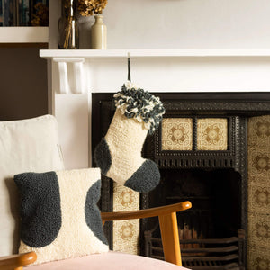 Punch needle stockings hanging from a fireplace with a matching punch needle cushion in front