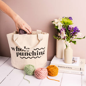Hand pulling yarn out of a Whole Punching cotton project bag