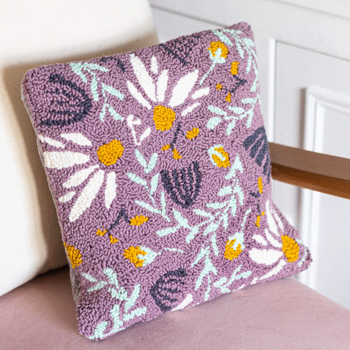 Lilac punch needle floral cushion propped against a pink velvet chair with a light cream cushion