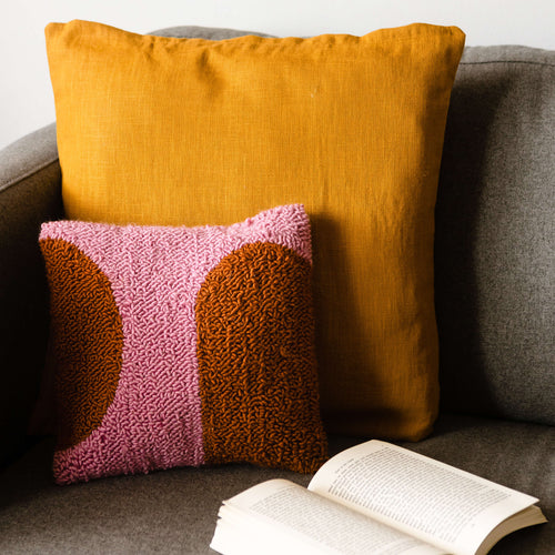 Pink and orange cushion propped on sofa with open book