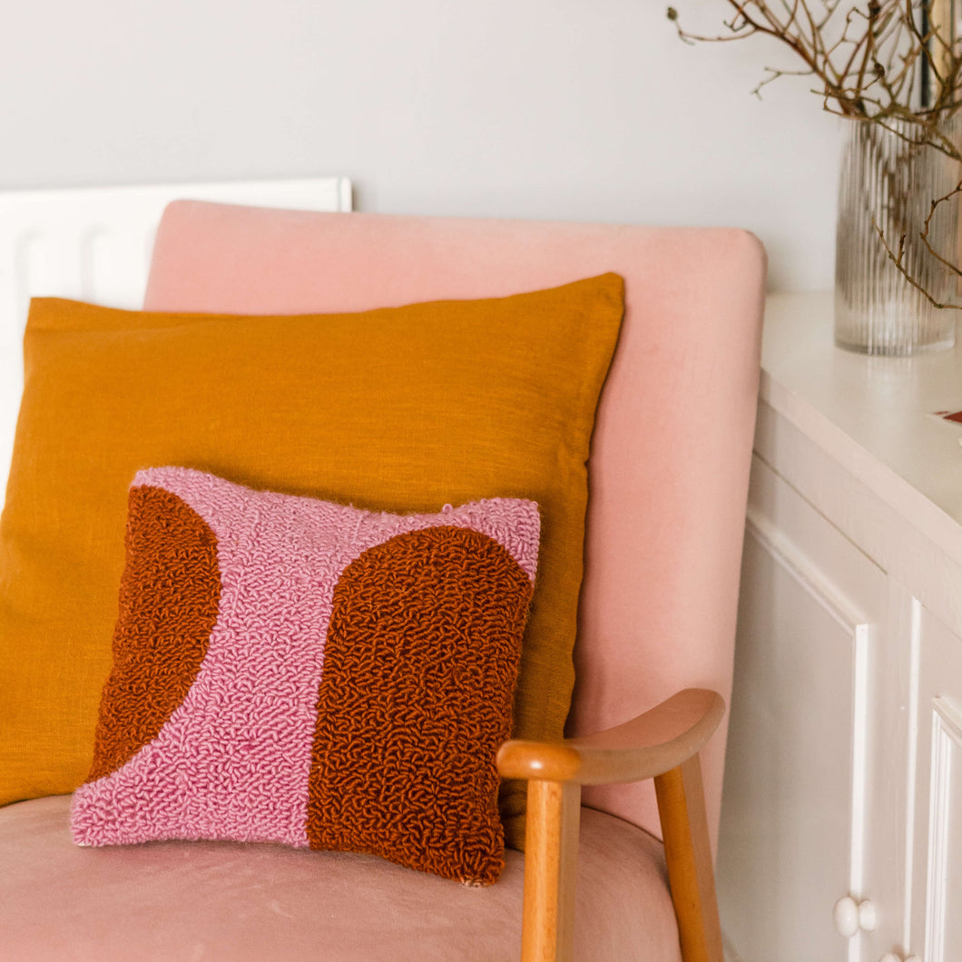 Pink and orange punch needle cushion propped on a pink chair with orange cushion behind